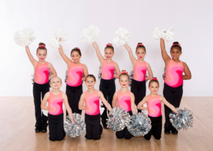 Pom class showing high and low diagonal in pink leotard and silver and white pompons